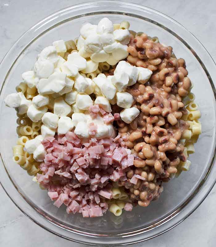 In a large glass serving bowl, mixing the ham, beans, and mozzarella into the pasta.