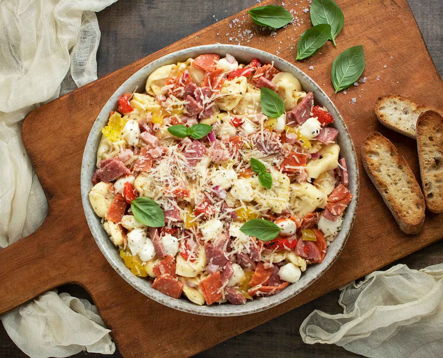 Overhead view of a bowl of Italian Grinder Tortellini Salad on a wooden serving board.