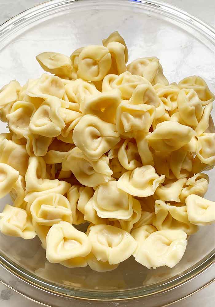 Cooled and drained tortellini in a glass mixing bowl.