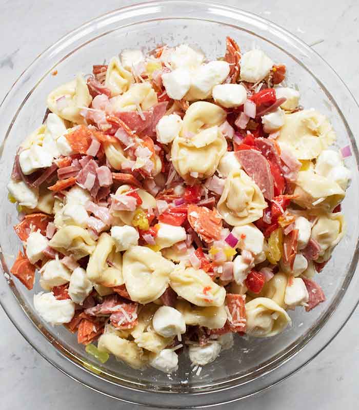 Finishing the tortellini salad with cheeses and dressing.