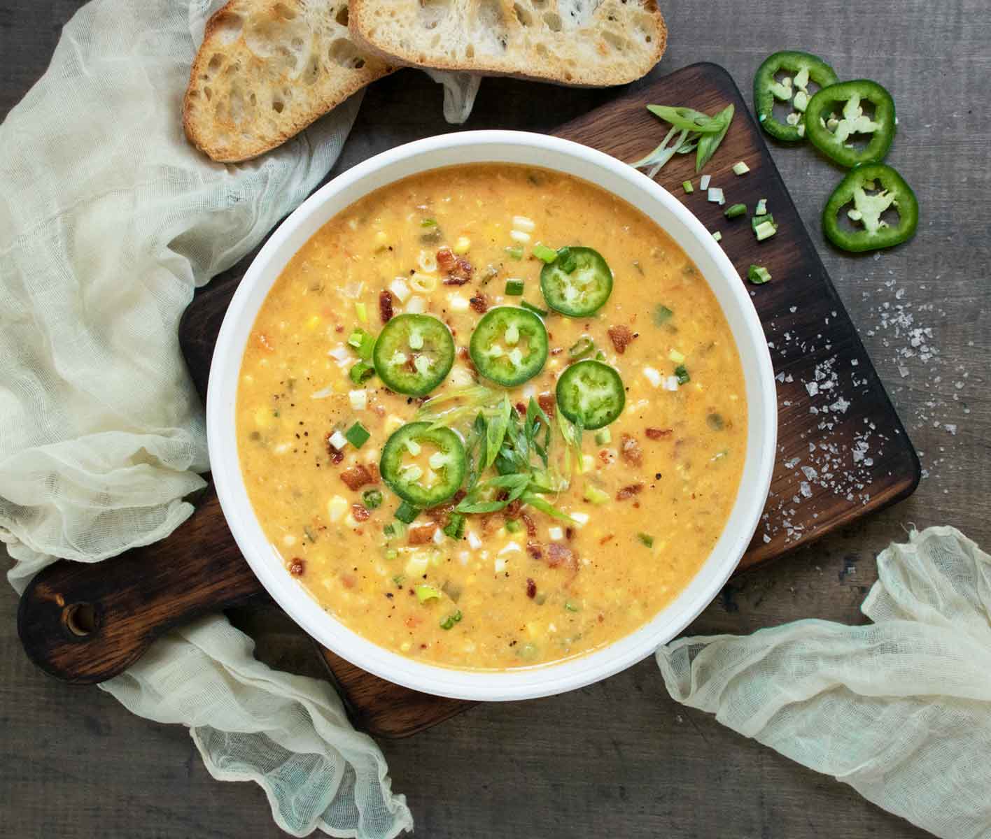 Jalapeno Bacon Corn Chowder in a white bowl on a wooden serving board.