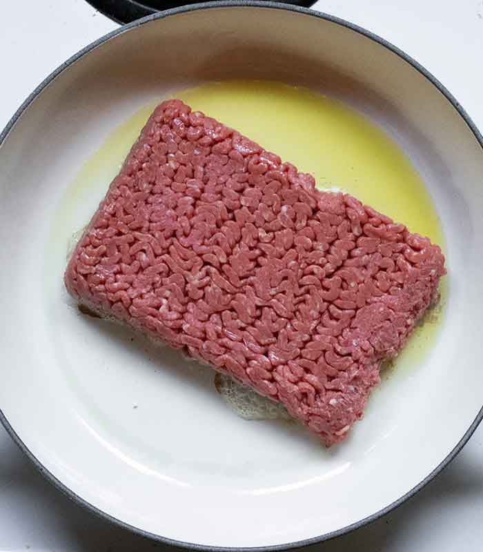 Fresh ground beef added to the hot pan.