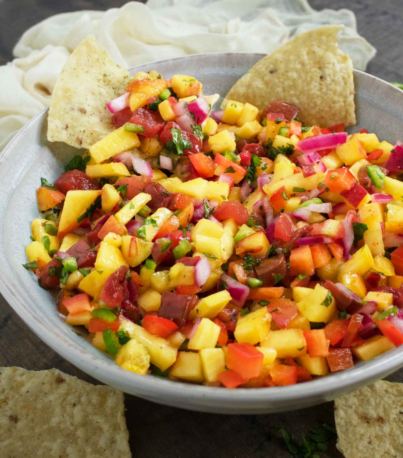 Side-angled view of peach salsa in a bowl with tortilla chips lined along the edge of the salsa.