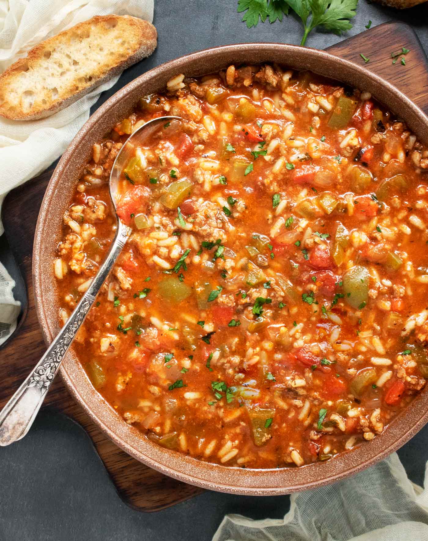 A bowl of Stuffed Pepper Soup on a wooden serving board with a slice of bread.