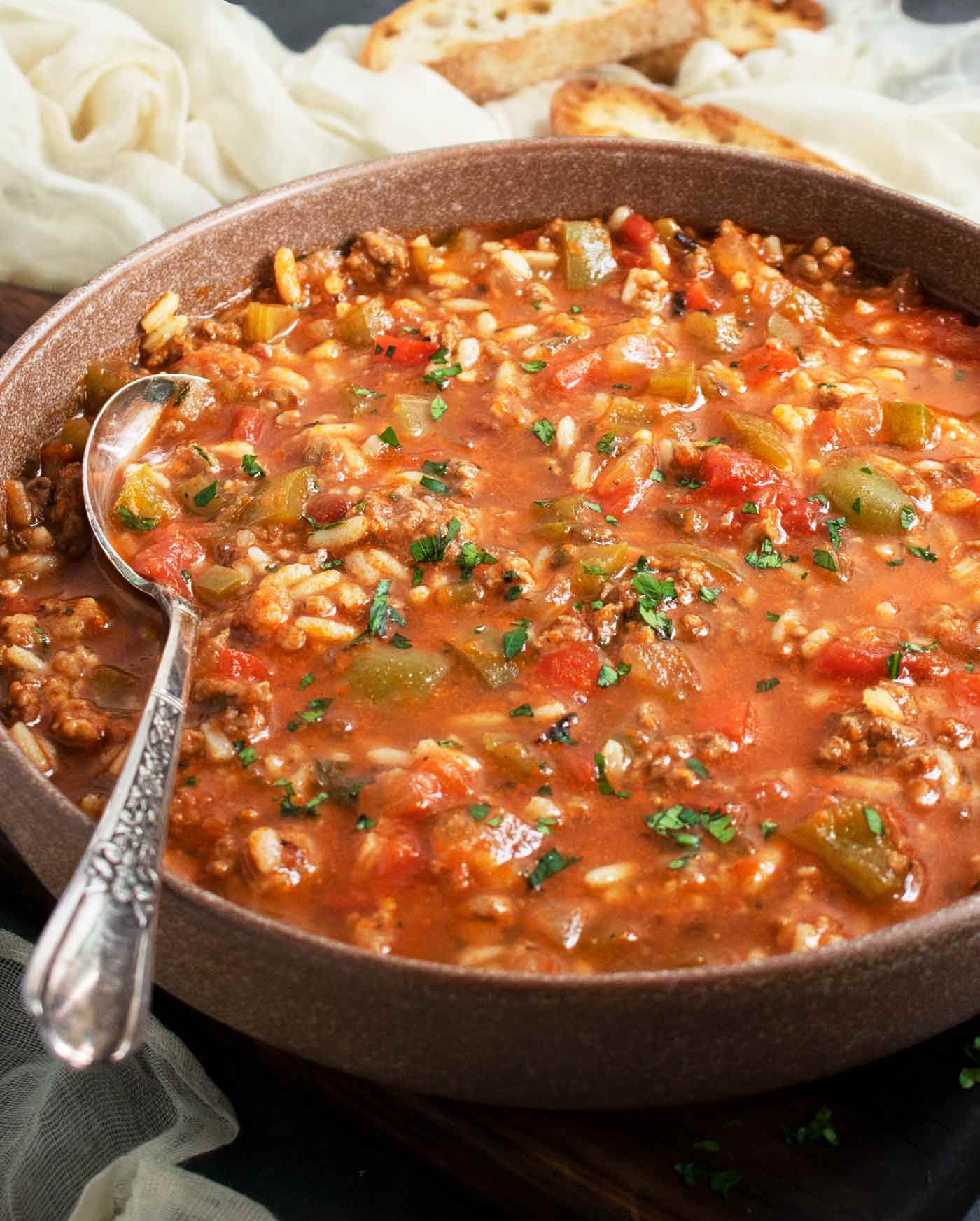 Side-angled view of Stuffed Pepper Soup in a reddish-brown bowl with a soup spoon.