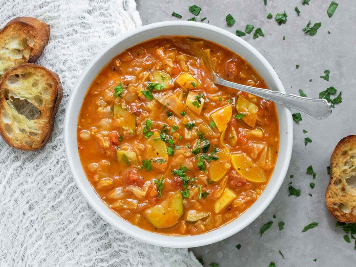 A bowl of Summer Cabbage Soup with a spoon and bread slices.