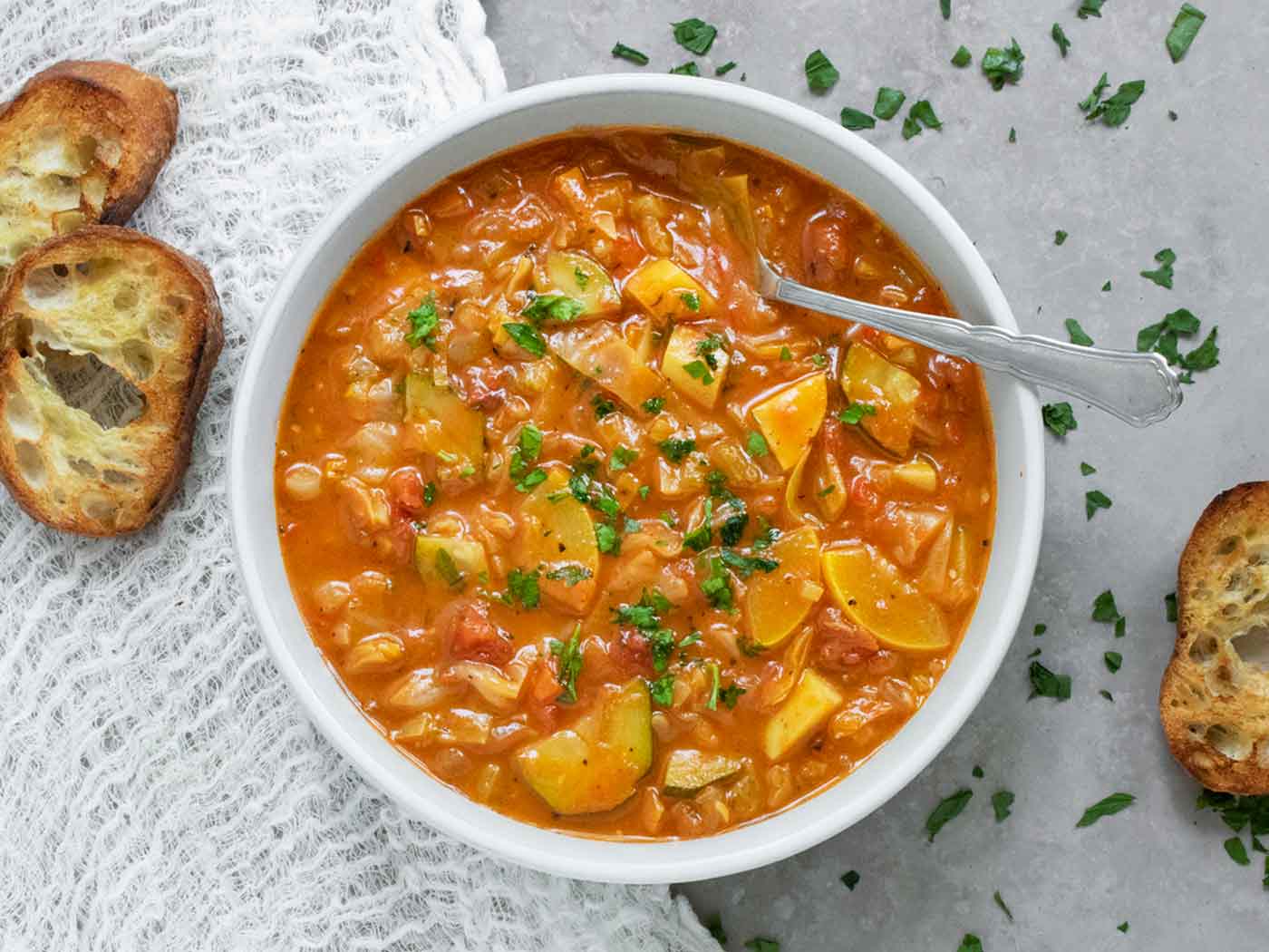 A bowl of Summer Cabbage Soup with a spoon and bread slices.