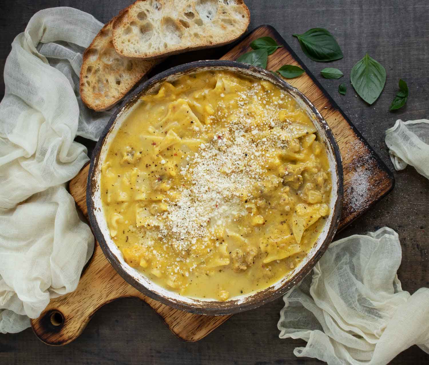 Butternut Squash Lasagna Soup in a rustic, white ceramic bowl, on a wooden serving board, with slices of toasty bread on the side.