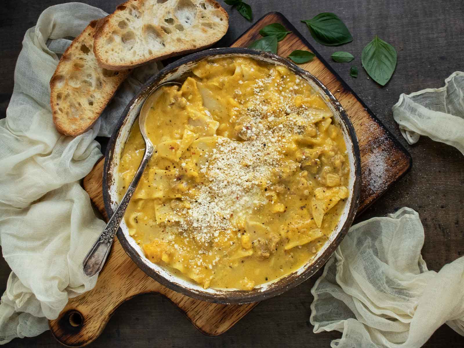 Butternut Squash Lasagna Soup in a rustic ceramic bowl with a spoon, on a wooden serving board.