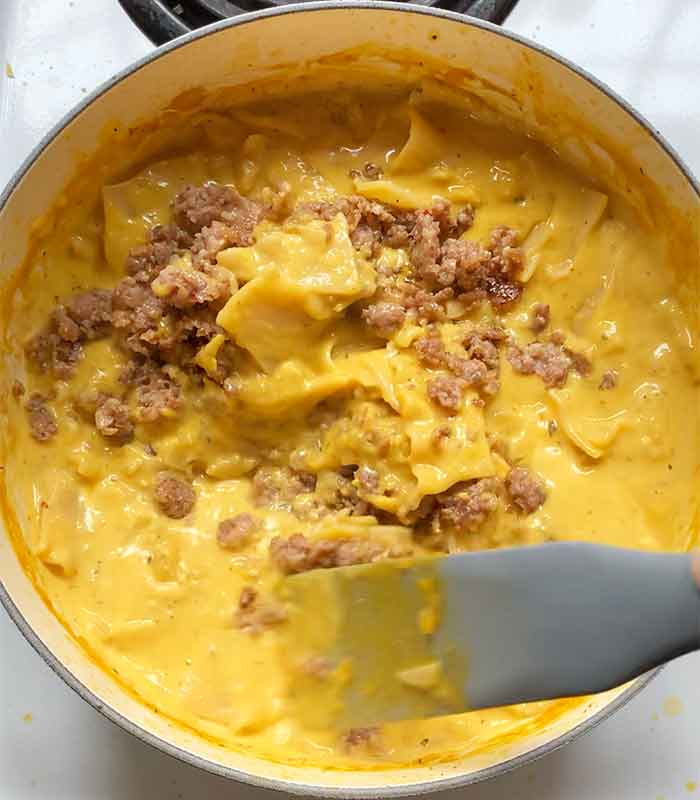 Returning the cooked sausage to the pot and mixing it into the soup.