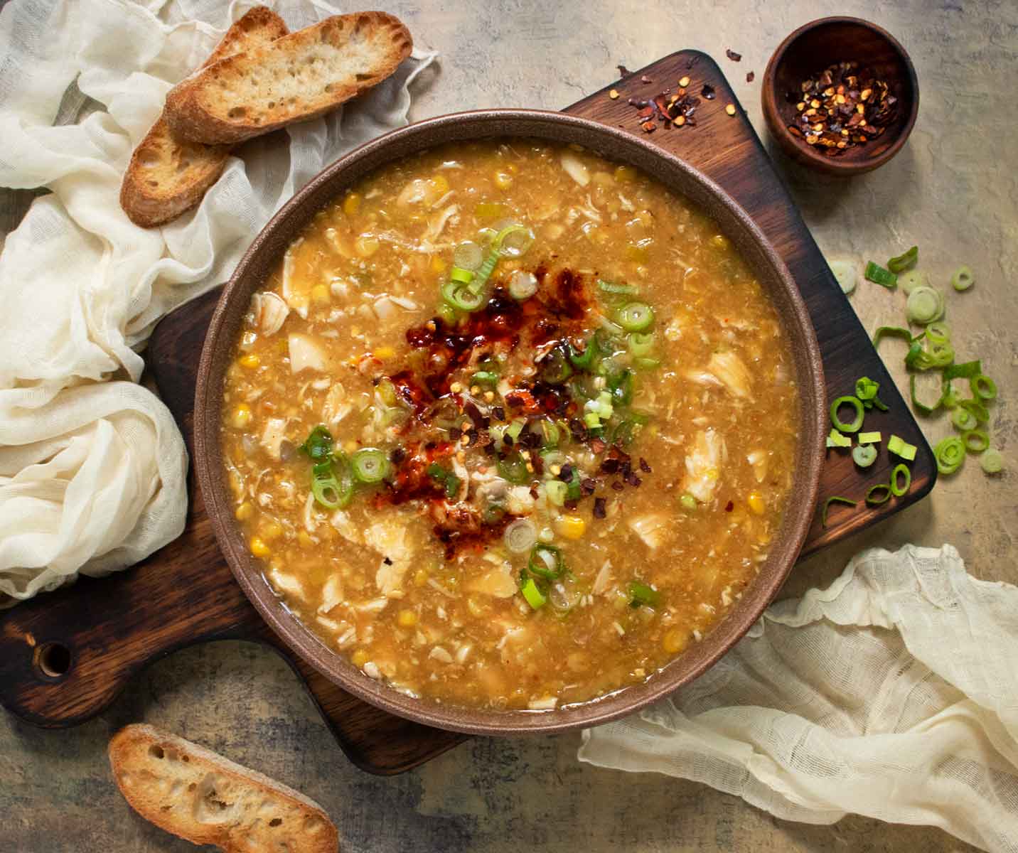 Overhead view of Creamy Chicken and Corn Soup in a brown bowl on a wooden serving board.