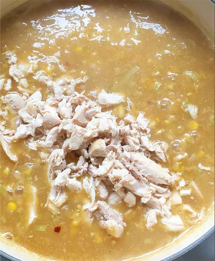 Adding the shredded rotisserie chicken to the soup.