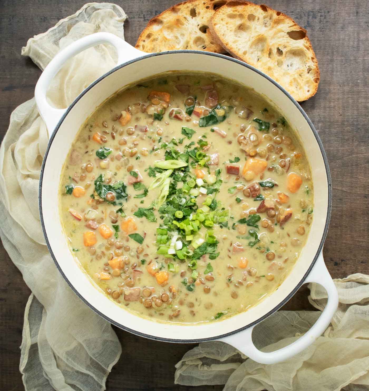 Overhead view of Green Curry Lentil Soup in a large white Dutch oven with toasty bread slices on the side.