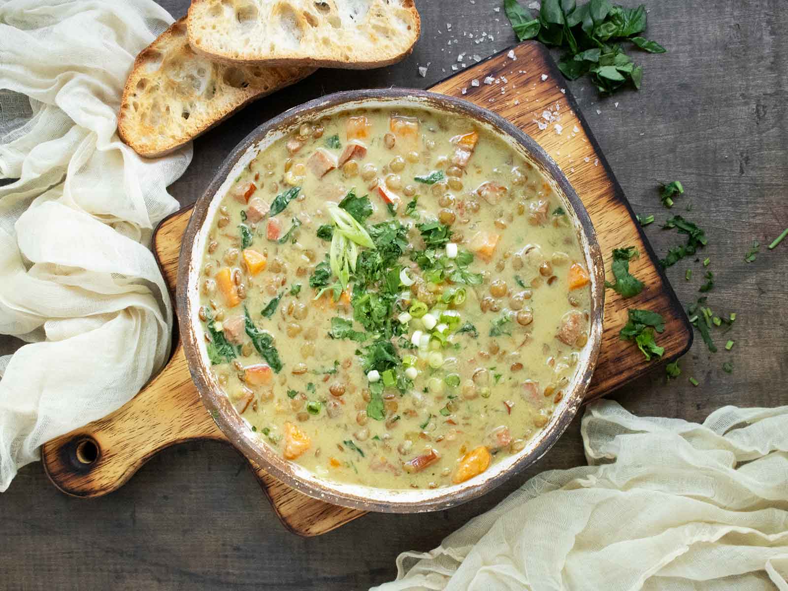 Overhead view of Green Curry Lentil Soup in a rustic ceramic bowl on a wooden serving board.