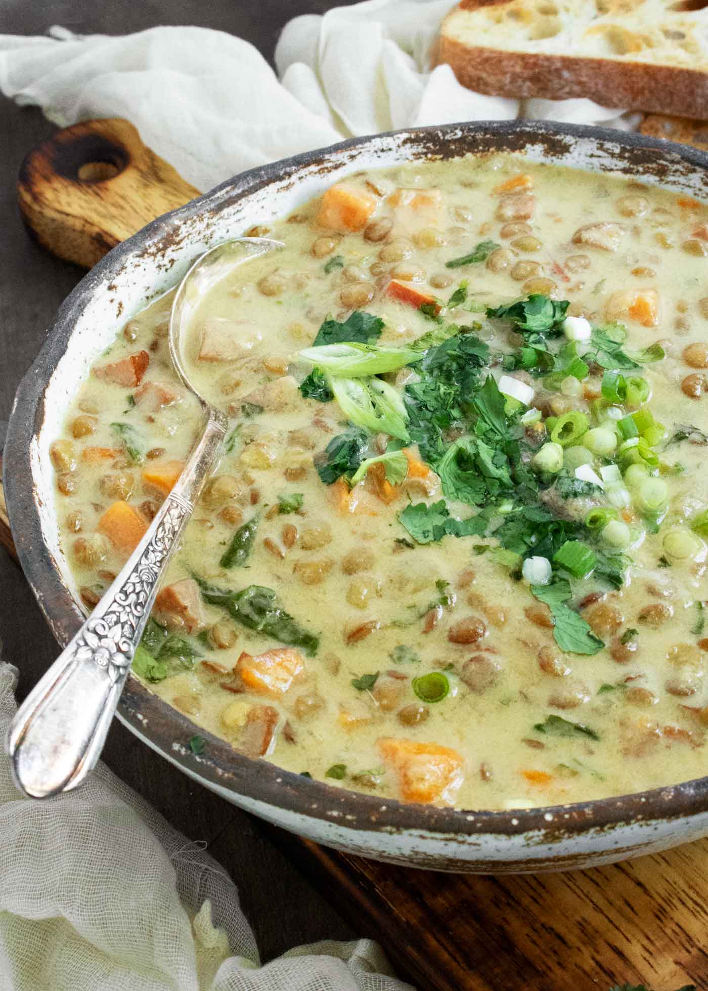 Side-angled view of Green Curry Lentil Soup in a white, rustic ceramic bowl with a spoon.