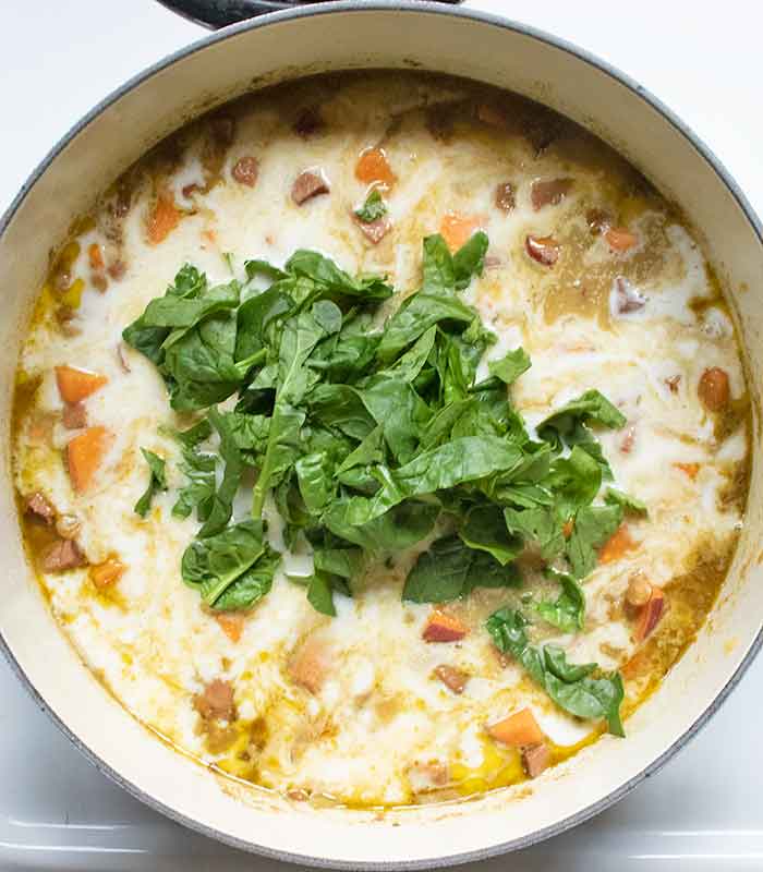 Finishing the soup by stirring in the coconut milk and spinach, and letting them warm through.