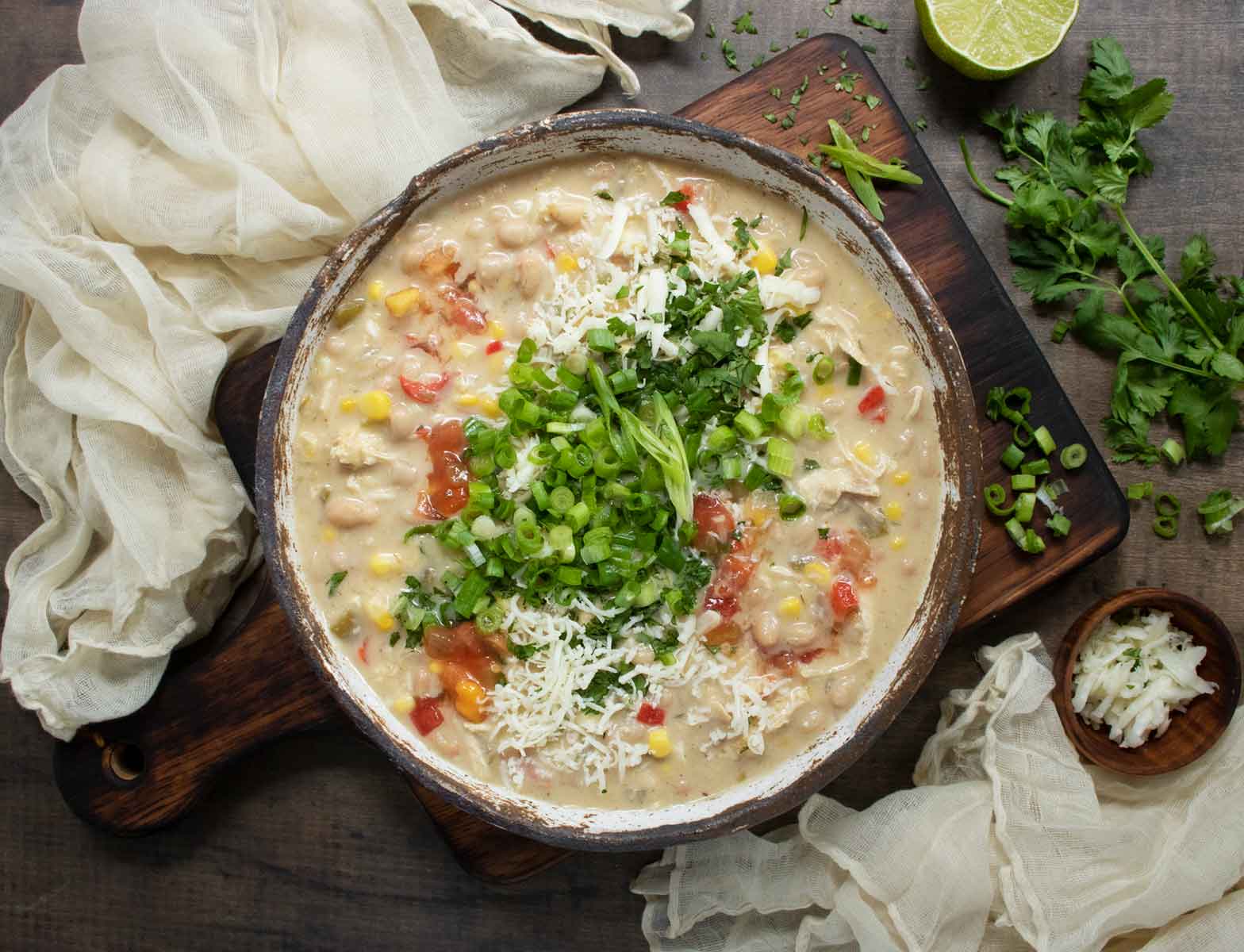 An overhead view of Southwest White Chicken Chili in a rustic ceramic bowl on a wooden serving board.