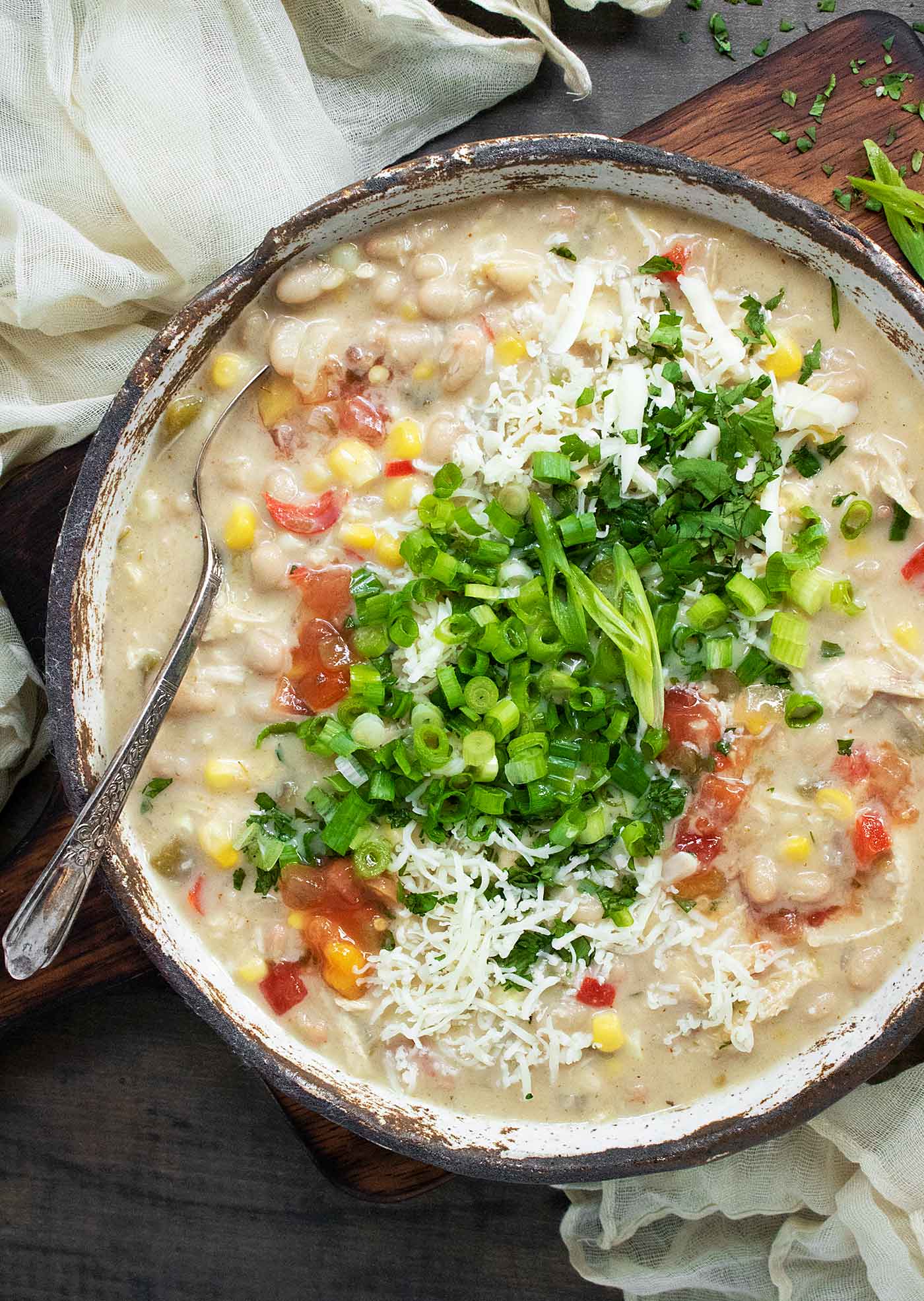 Overhead view of Southwest White Chicken Chili in a rustic, white ceramic bowl, with a spoon.