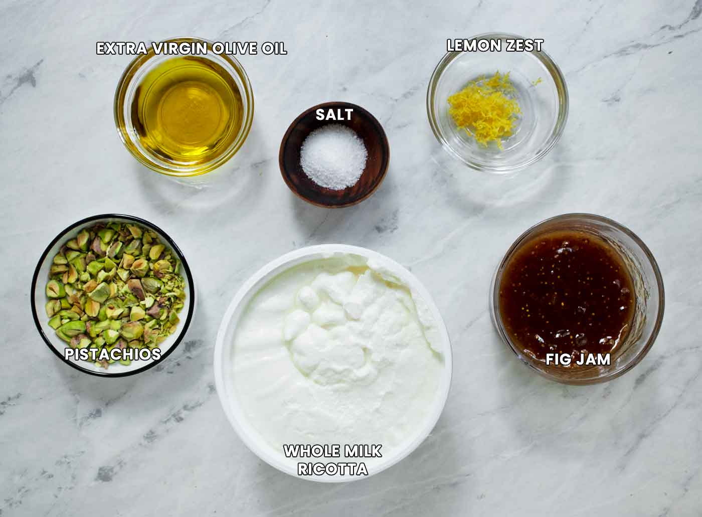 Prepped ingredients for the dip in individual containers on a white marble board.