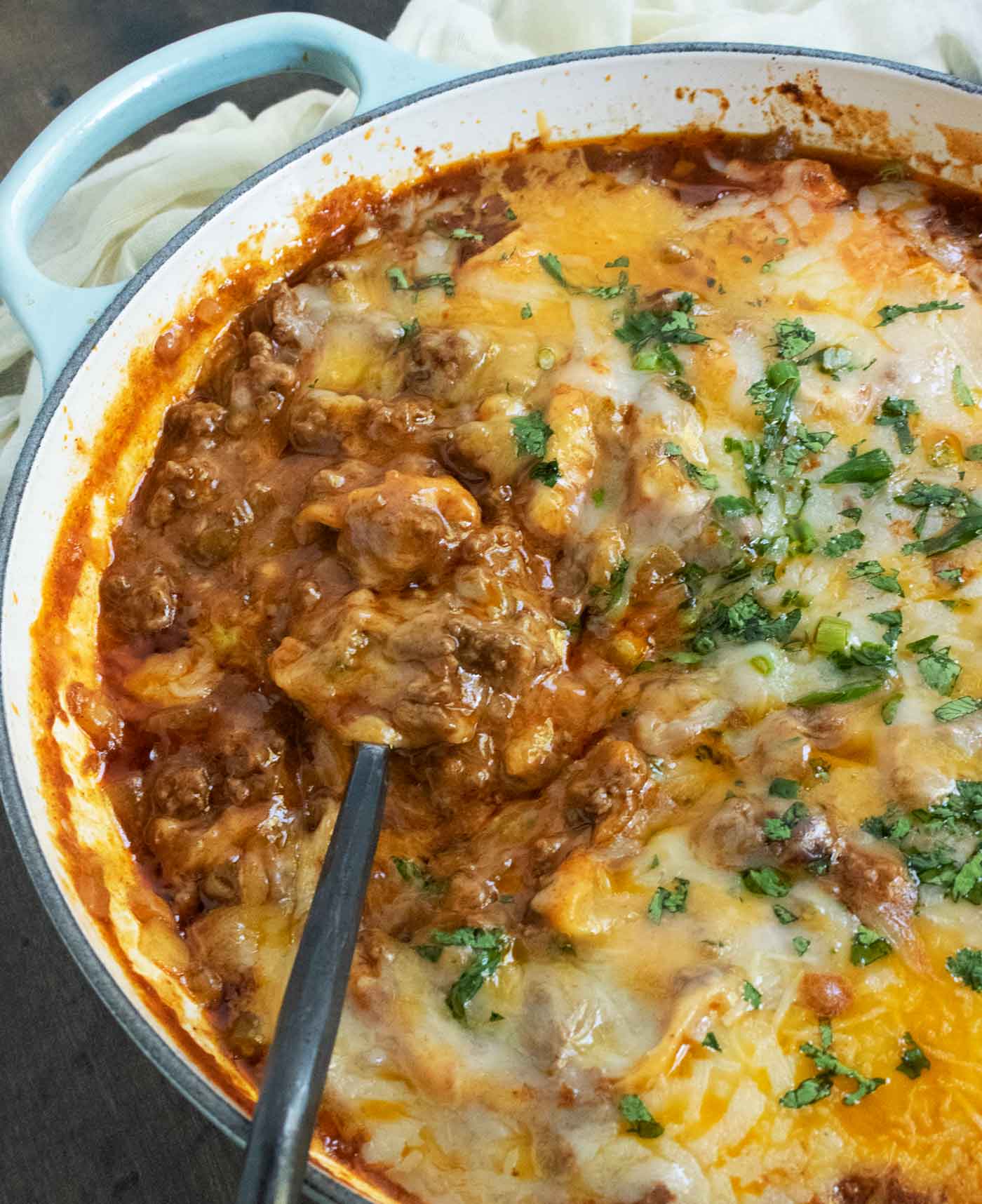 Side-angled view of Cheesy Beef Enchilada Skillet in a braiser with a serving spoon.