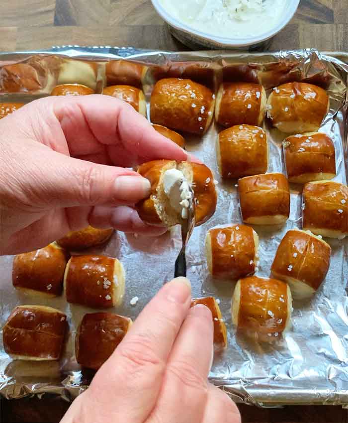 Spreading a small amount of cream cheese into the pretzel slice with a small spoon.