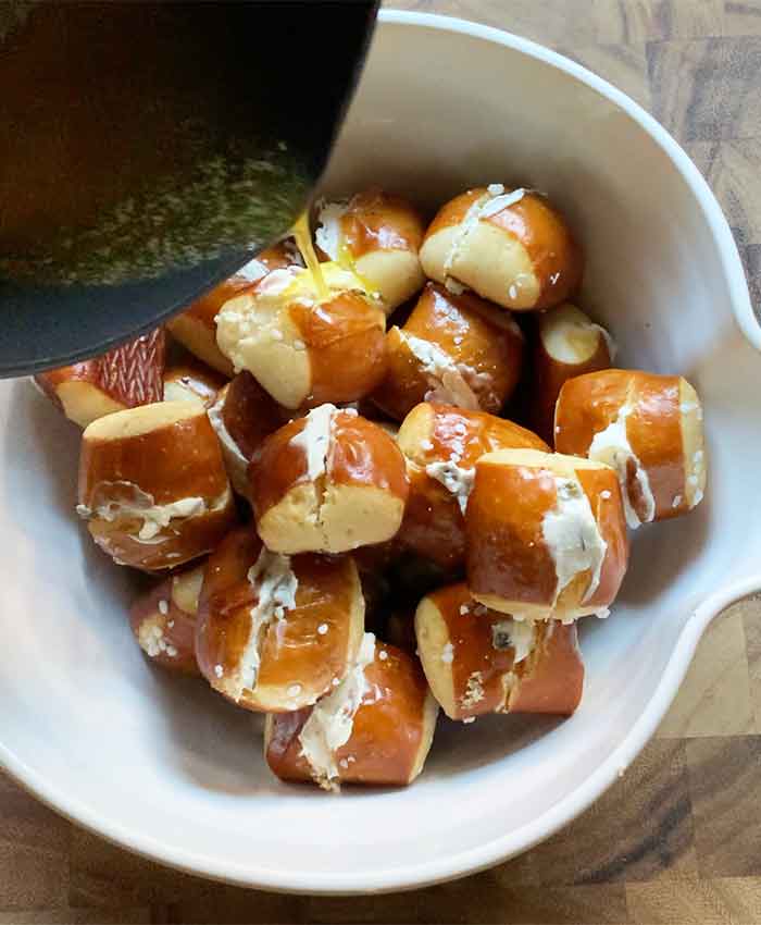 Pouring the ranch butter over the stuffed pretzel bites in a large mixing bowl.