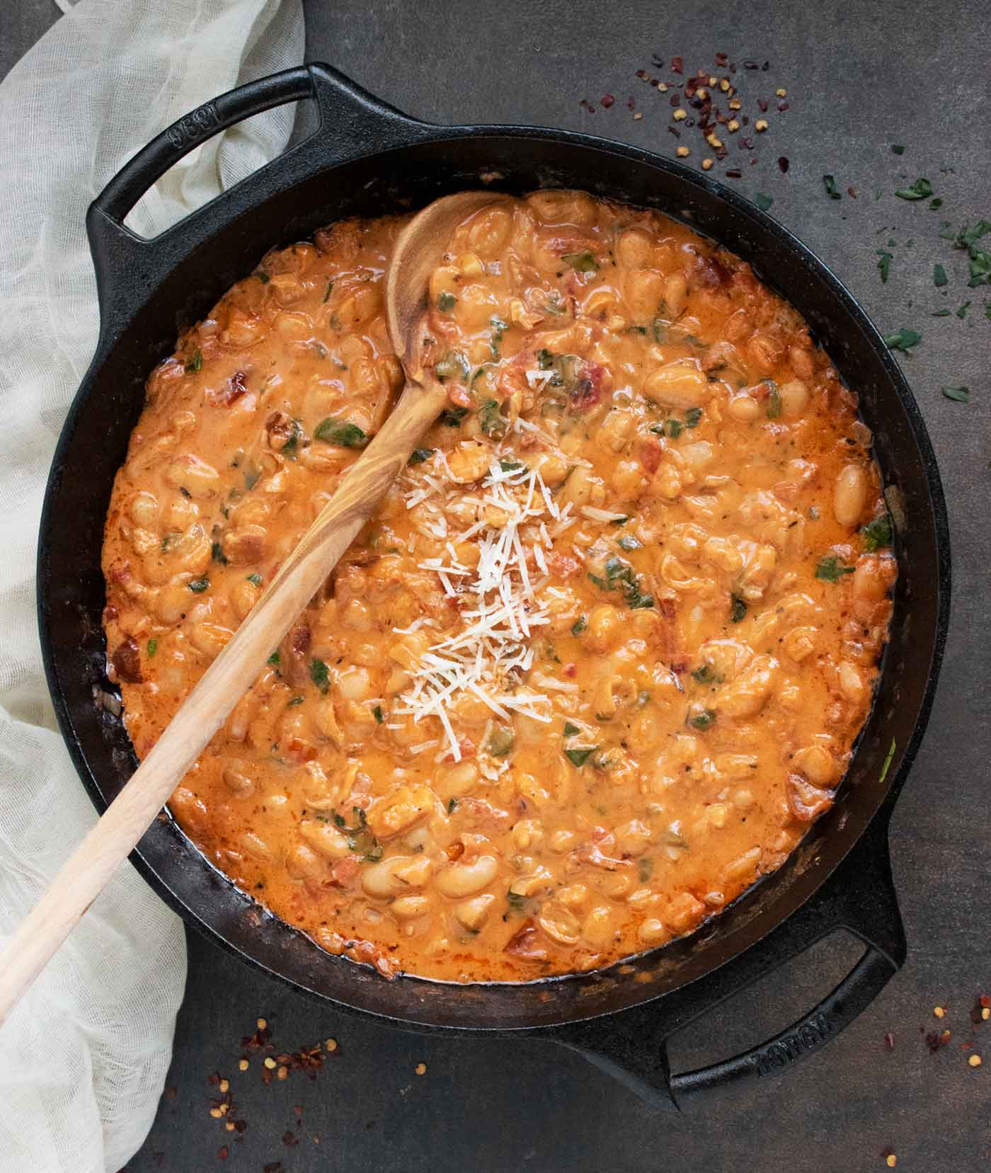 Overhead view of Marry Me White Beans in a large cast iron skillet with a long wooden serving spoon.