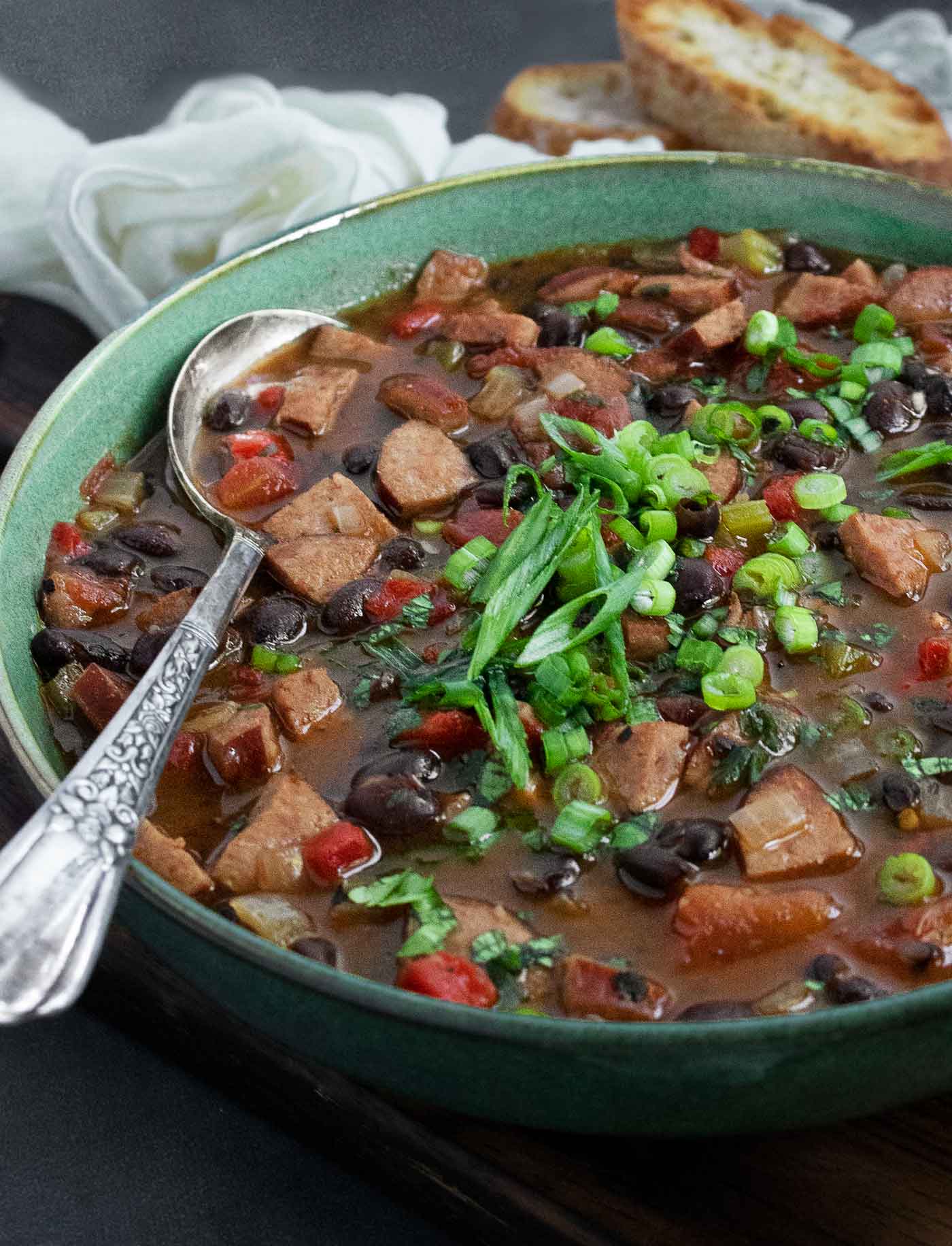 Side-angled view of a bowl of Smoky Black Bean and Sausage Soup with a spoon.