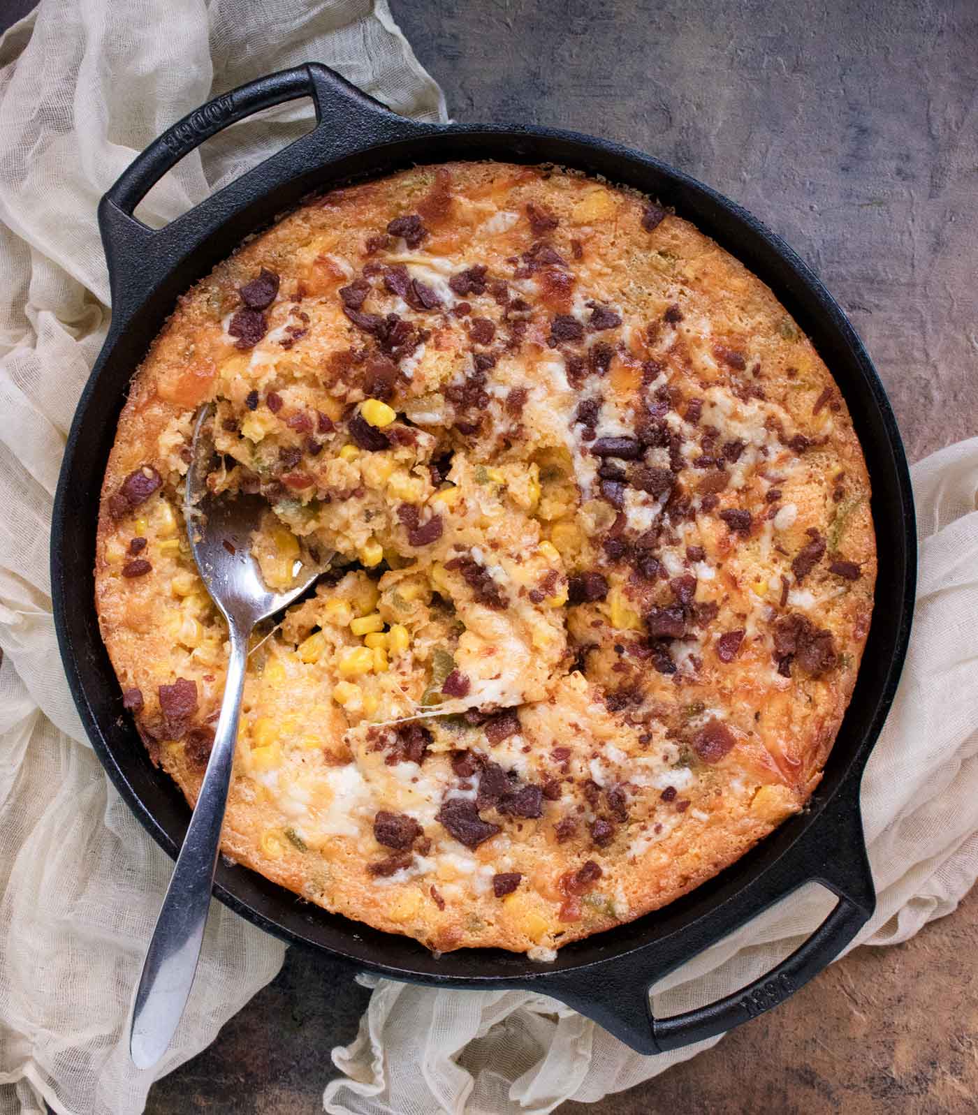 Overhead view of Jalapeno Corn Casserole in a cast iron skillet with a serving spoon.