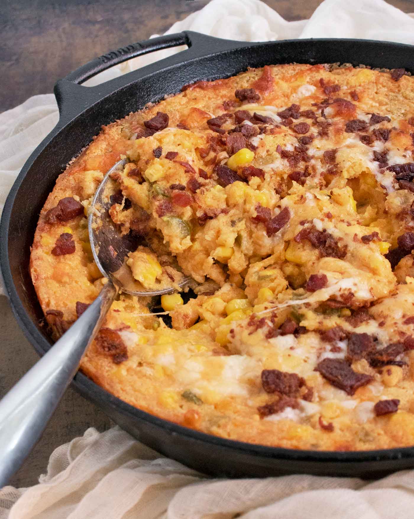 Side view of the skillet of Jalapeno Corn Casserole with a serving spoon.