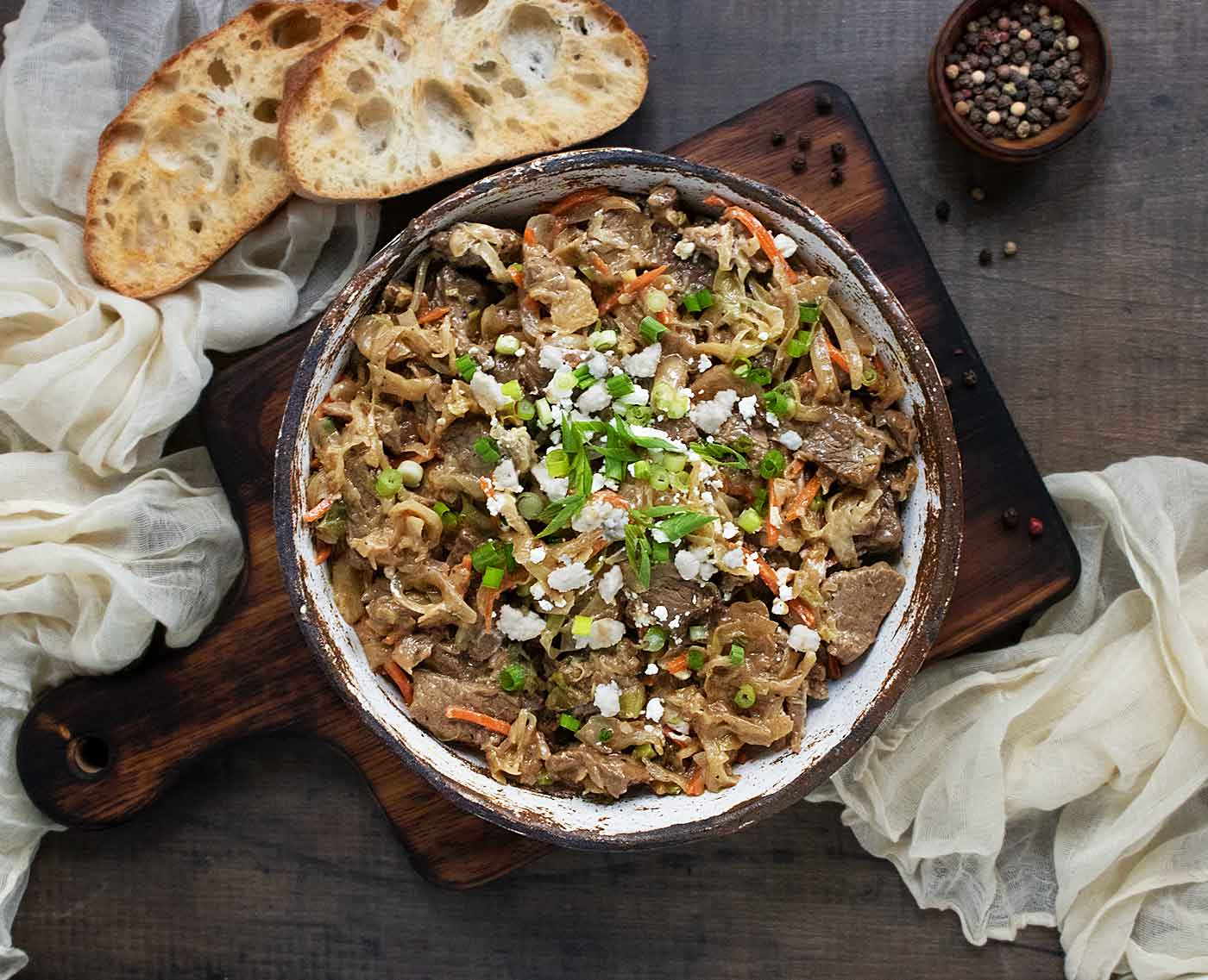 Overhead view of Steak and Cabbage in a rustic white bowl with a side of bread.