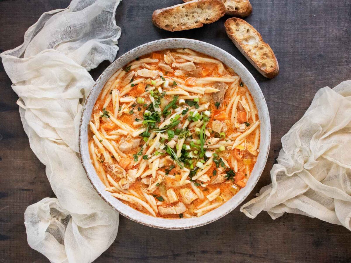 Overhead view of Thai Fusion Chicken Noodle Soup in a bowl with bread slices on the side.