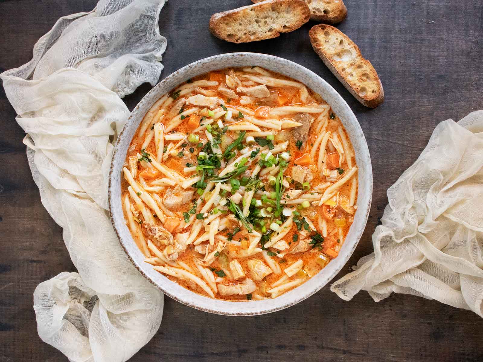 Overhead view of Thai Fusion Chicken Noodle Soup in a bowl with bread slices on the side.