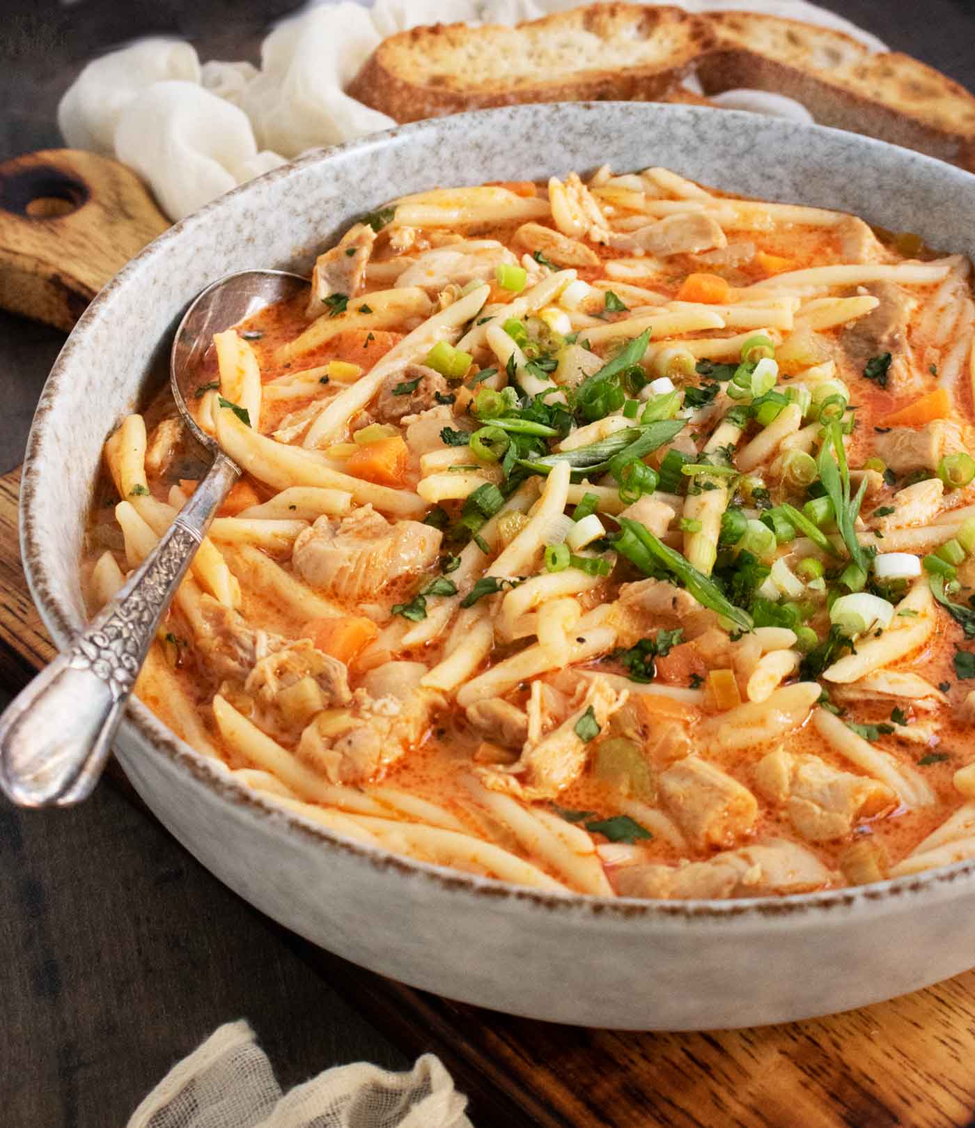 Side-angled view of a bowl of Thai Fusion Chicken Noodle Soup with a serving spoon.