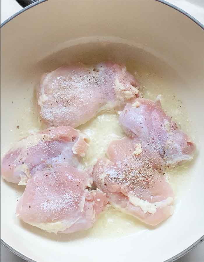 Chicken thighs cooking in oil in a Dutch oven.
