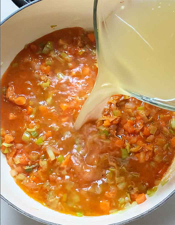 Chicken broth poured from a glass measuring cup into the soup pot.