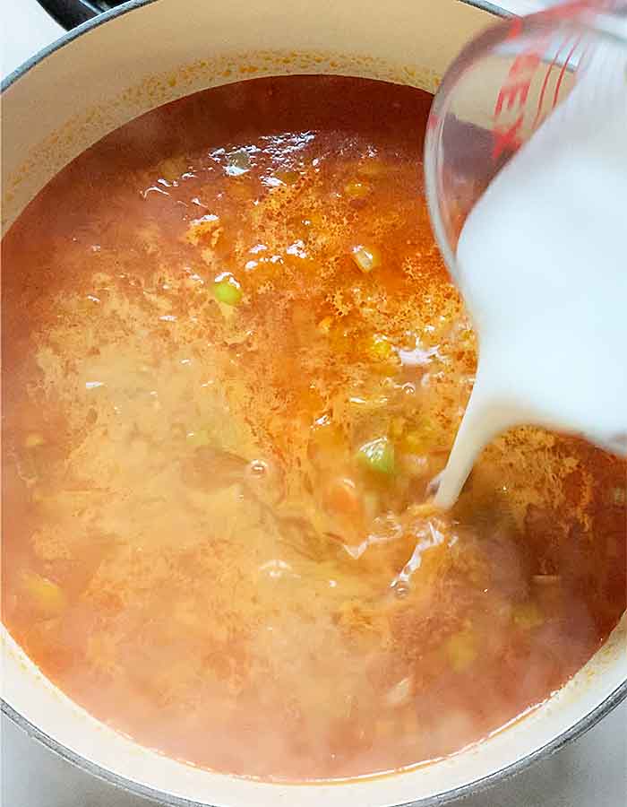Coconut milk poured from a smaller glass measuring cup into the soup.