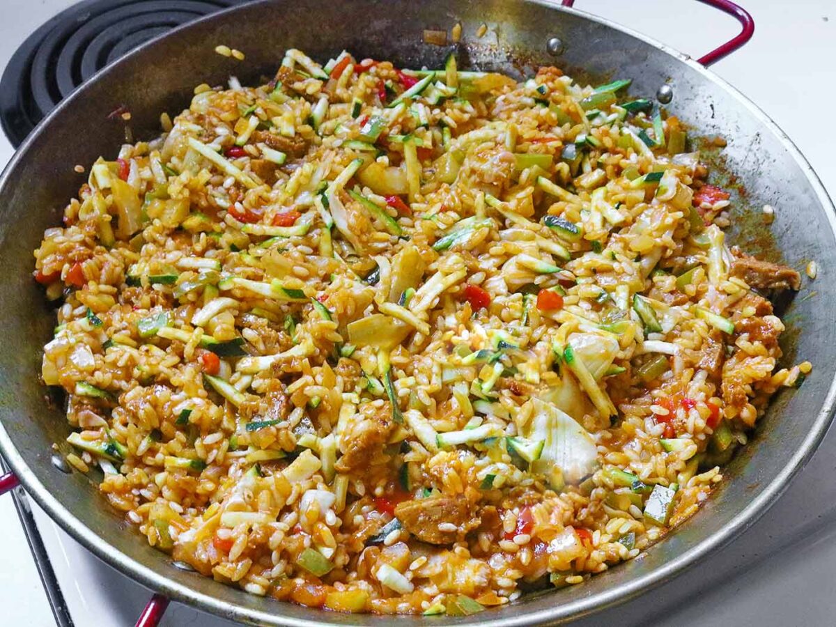 Vegetarian Paella in a carbon steel pan with red handles, on the stovetop.