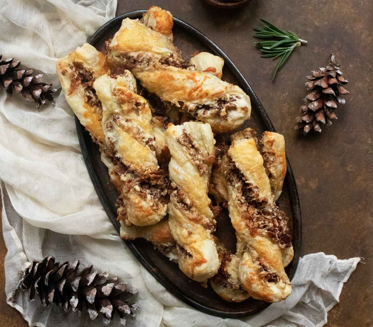 Overhead view of Cheesy Candied Bacon Twists stacked on a dark platter.