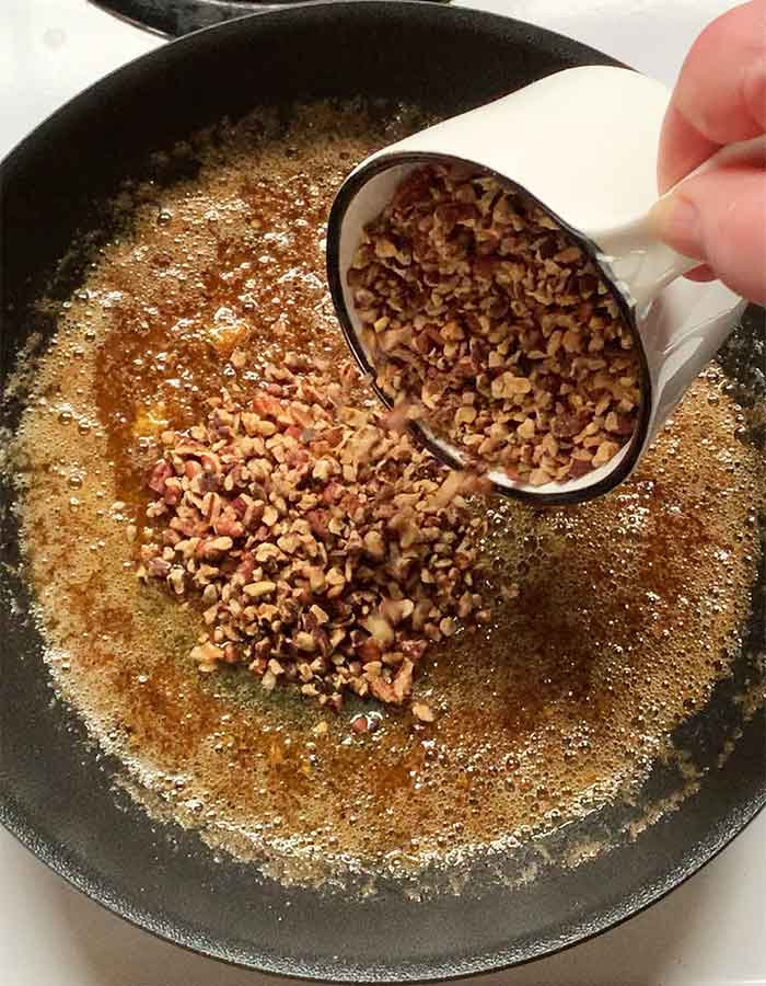 Pouring in the chopped pecans from. a white ceramic measuring cup to toast and cover with the glaze.