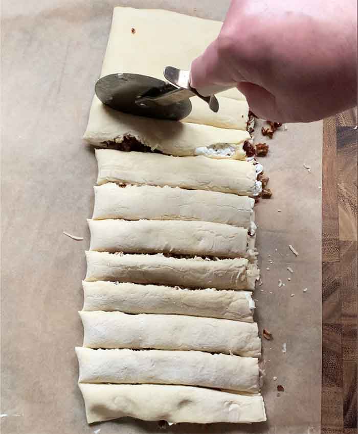 Using a pizza cutter to slice the filled dough into thin strips.