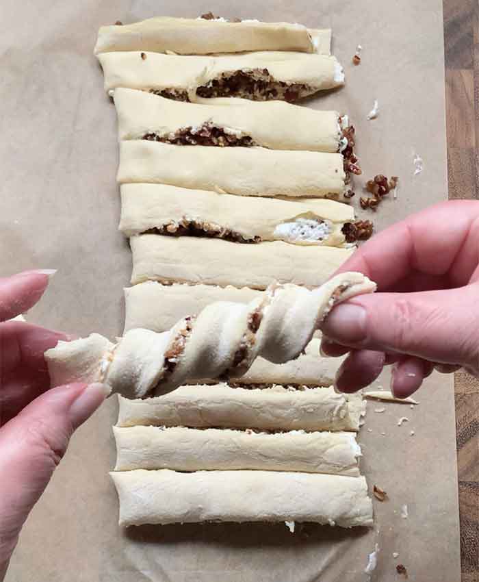 A close-up of my hands twisting one strip of filled dough into a spiral.