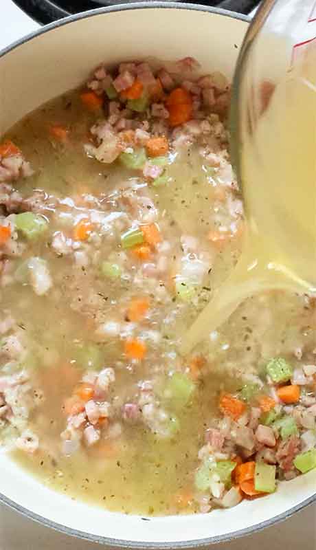 Adding chicken broth to the meat and vegetable mixture.