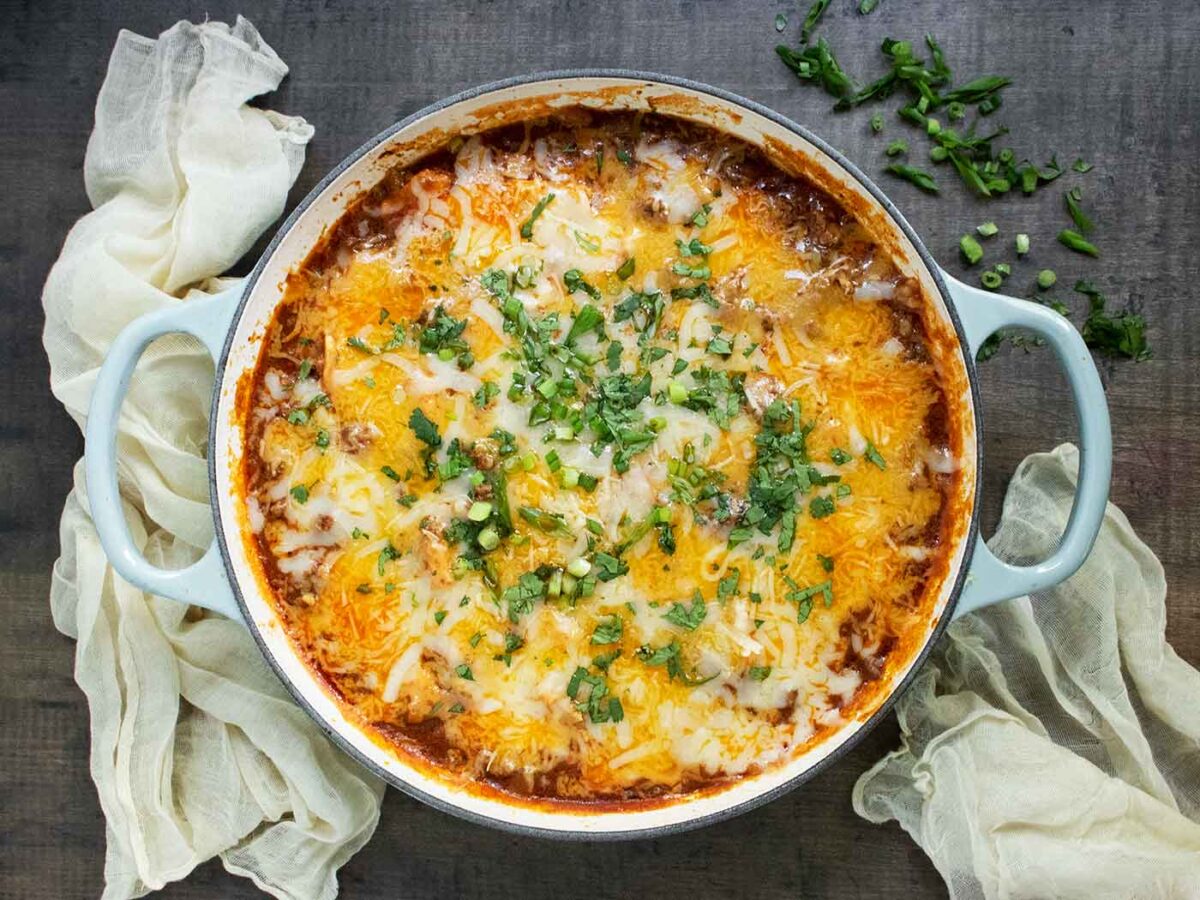 An overhead view of Cheesy Beef Enchilada Skillet in a braiser with light blue handles.