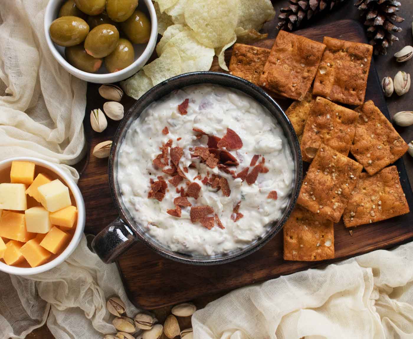Crispy Pepperoni Ranch Dip in a black bowl with a handle, set on a wooden serving board with chips, cheese cubes and olives.