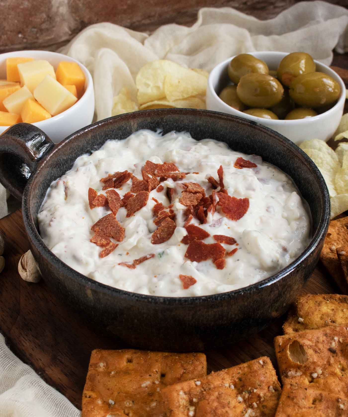 The finished and topped dip in a beautiful black ceramic bowl with a handle, set on a wooden board with chips.