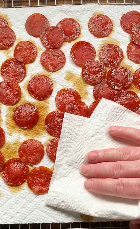 Blotting the pepperonis dry with a paper towel.