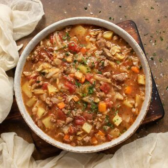 A bowl of Beef and Cabbage Soup on a wooden board.