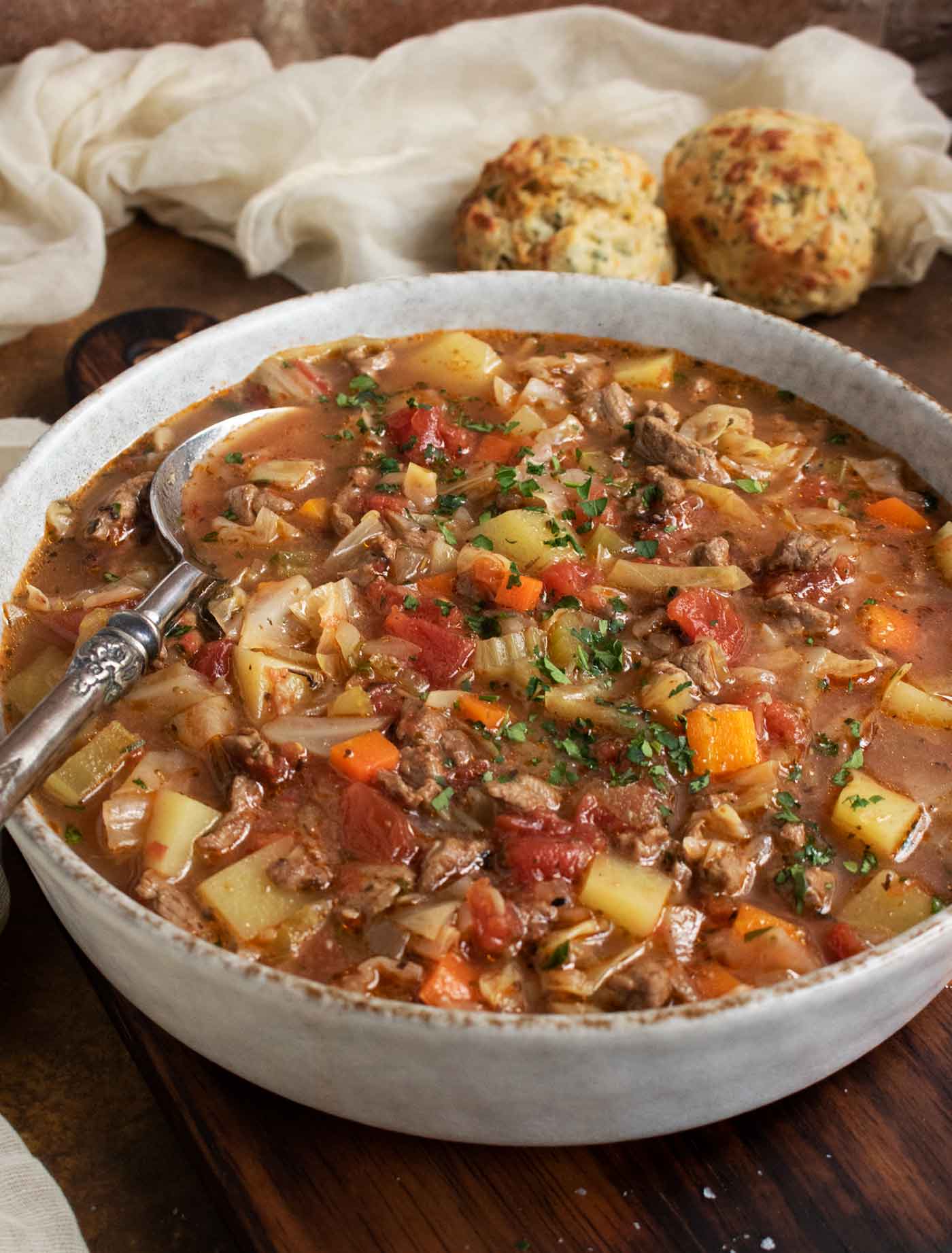 Side-angled view of a bowl of Beef and Cabbage Soup, with a spoon.