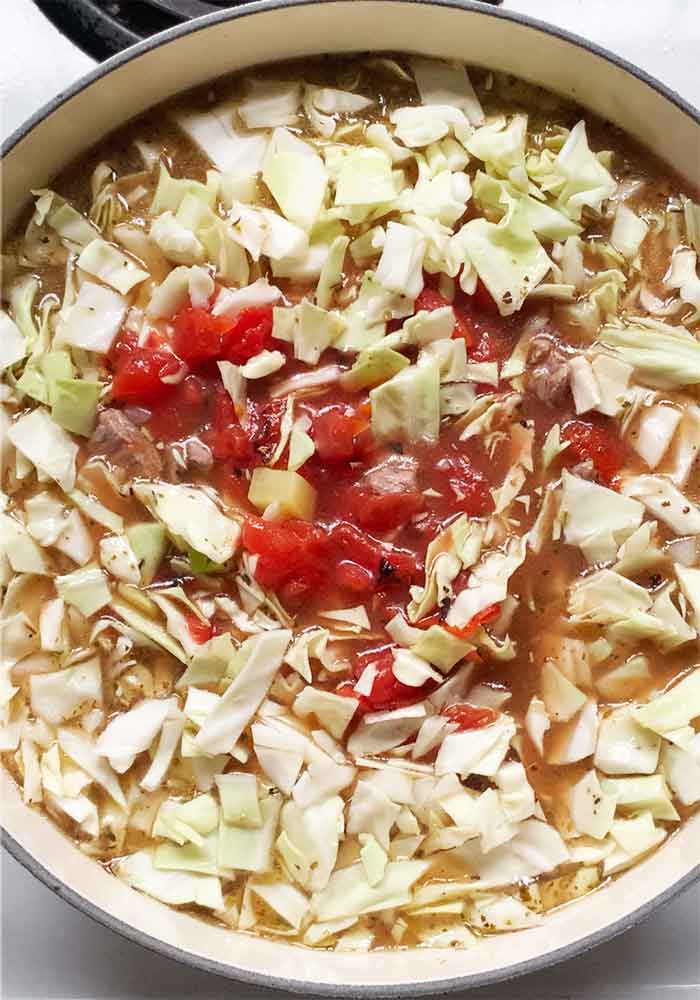 Adding the tomatoes and cabbage to the soup.